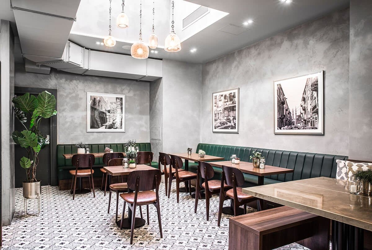 Wnętrze restauracji z zielonymi skórzanymi kanapami, drewnianymi stolikami i wzorzystą płytką na podłodze