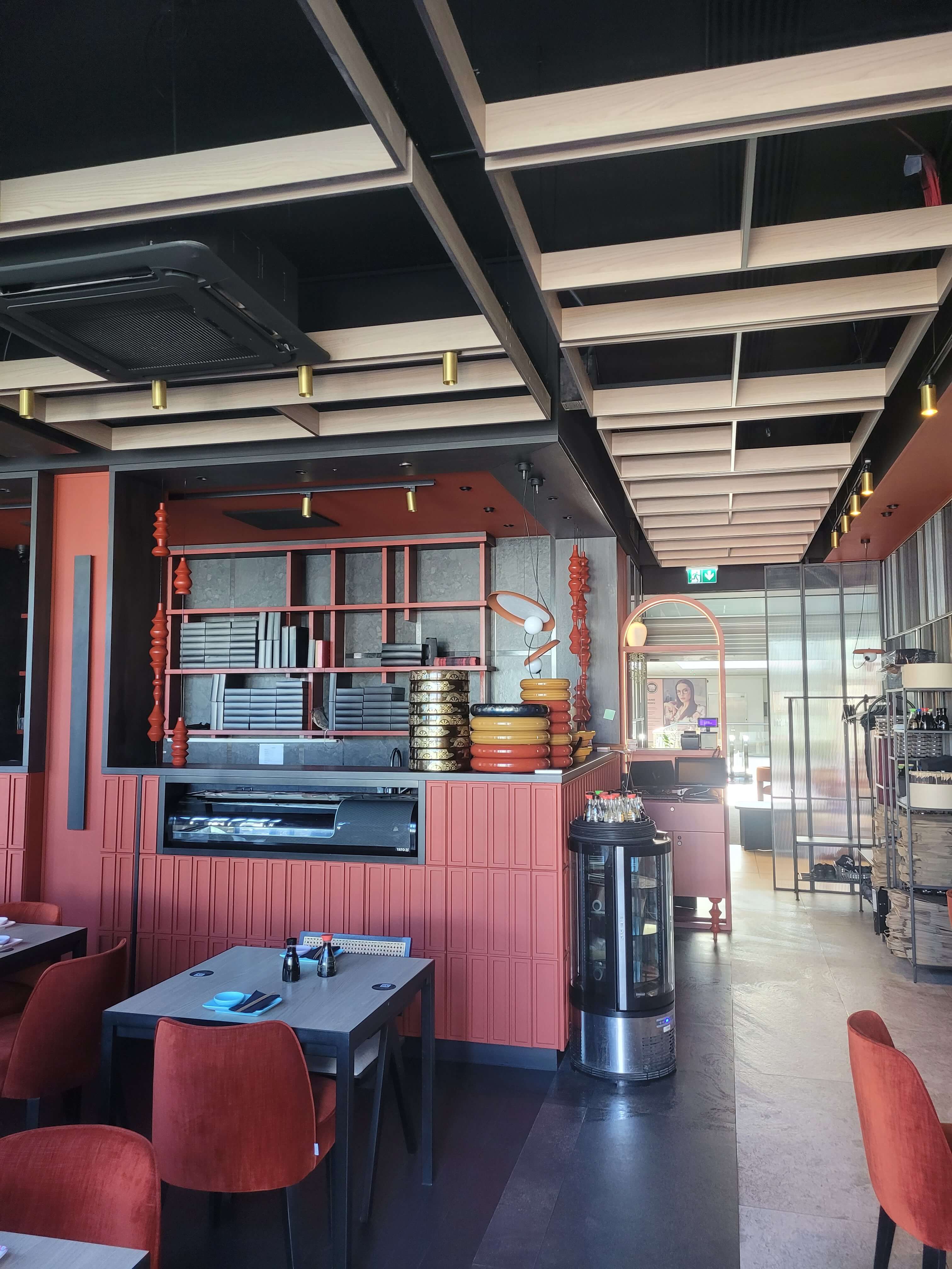 Wnętrze restauracji sushi z terakotowymi meblami, drewnianymi lamelami na suficie i barem sushi