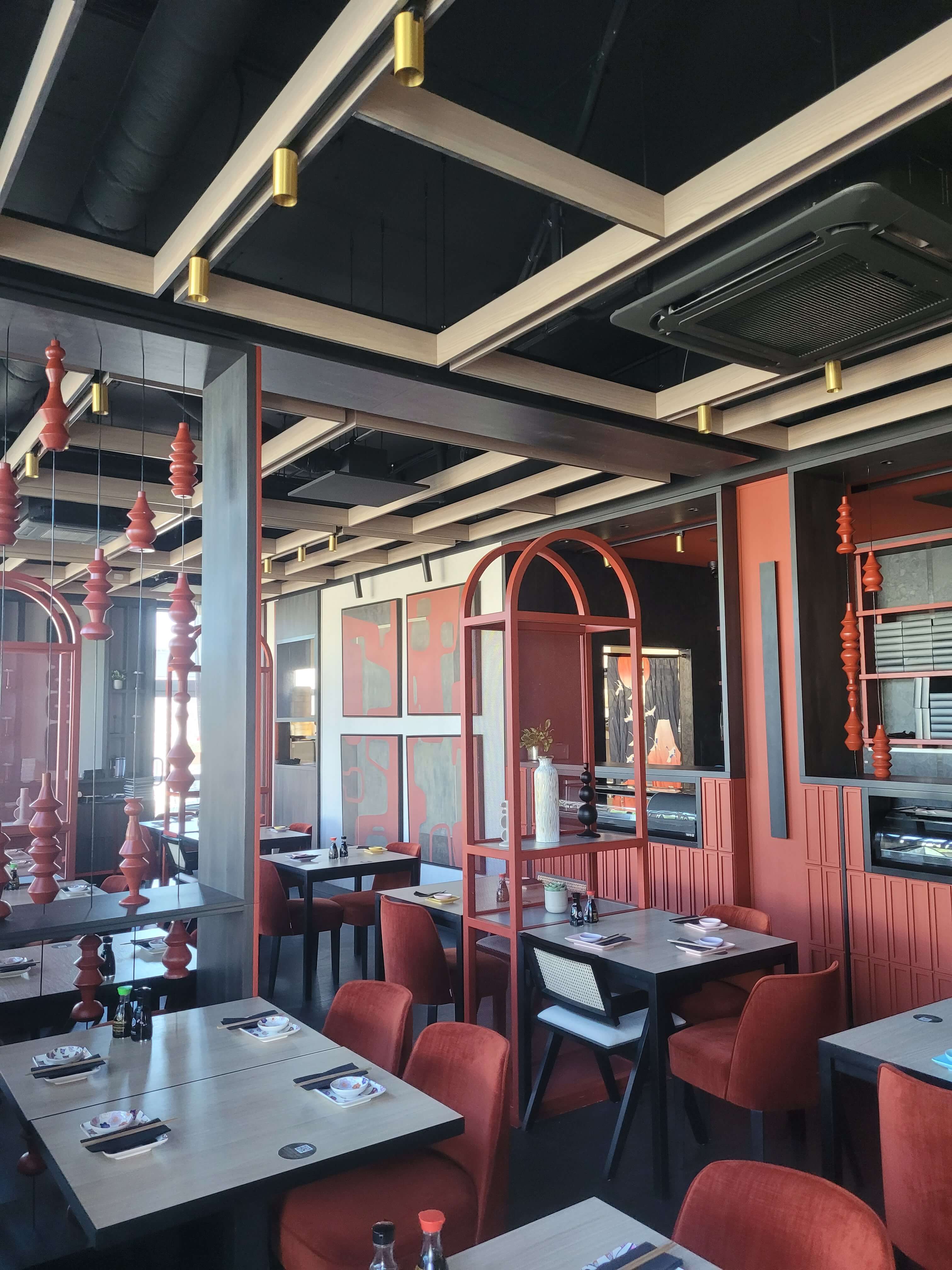 Sala restauracyjna z ceglastymi krzesłami, łukowymi metalowymi regałami i drewnianymi lamelami na suficie