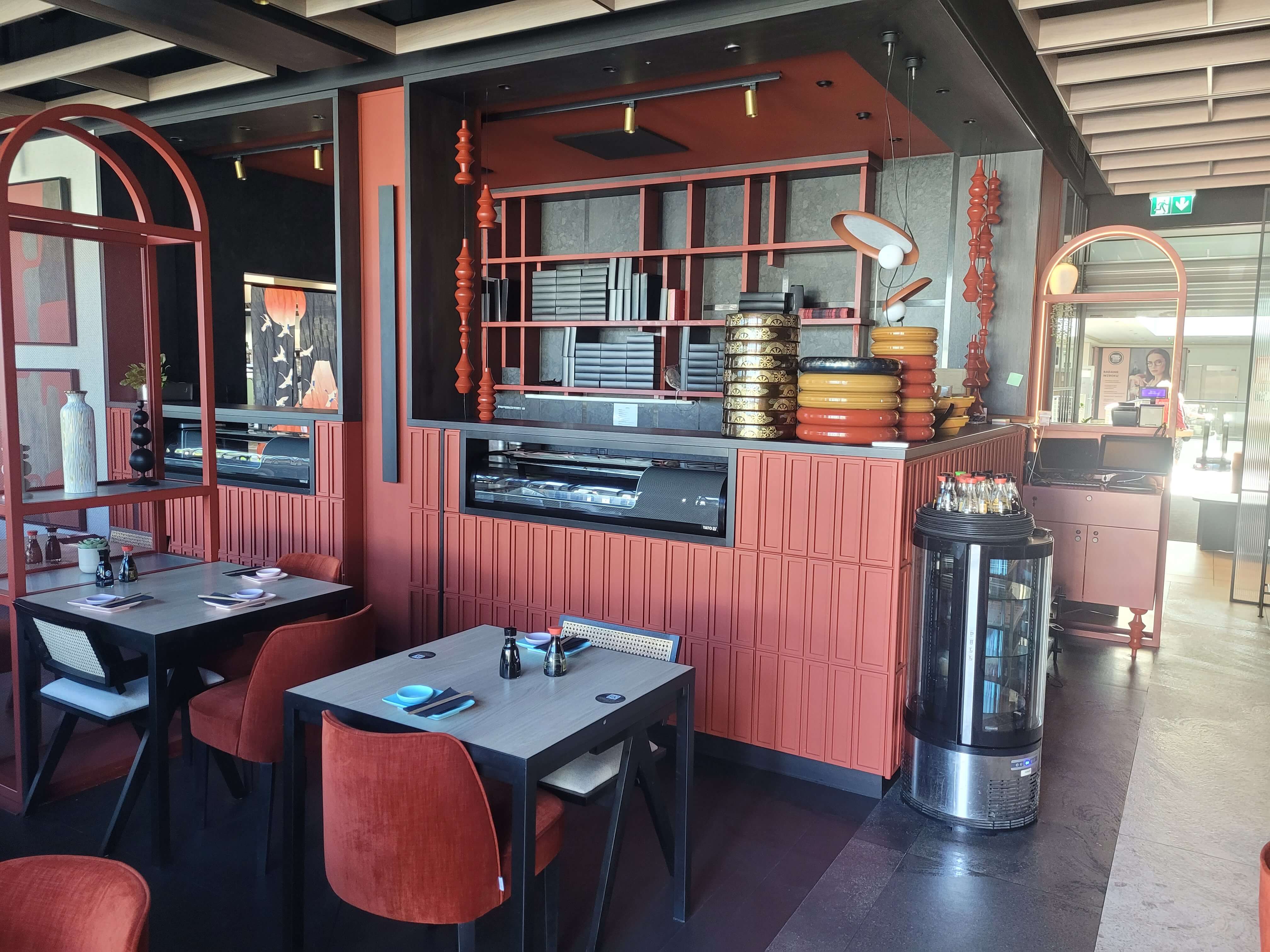 Bar sushi z terakotową zabudową, dekoracyjnymi regałami i witryną chłodniczą